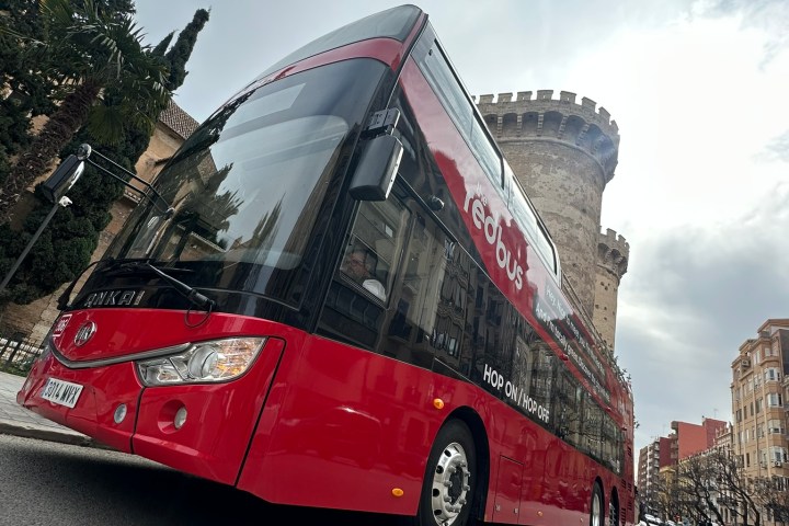 Red double-decker bus on a street near a historic stone tower.