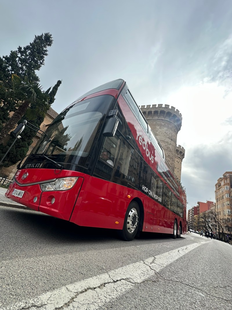 Red double-decker bus on a street near a historic stone tower.